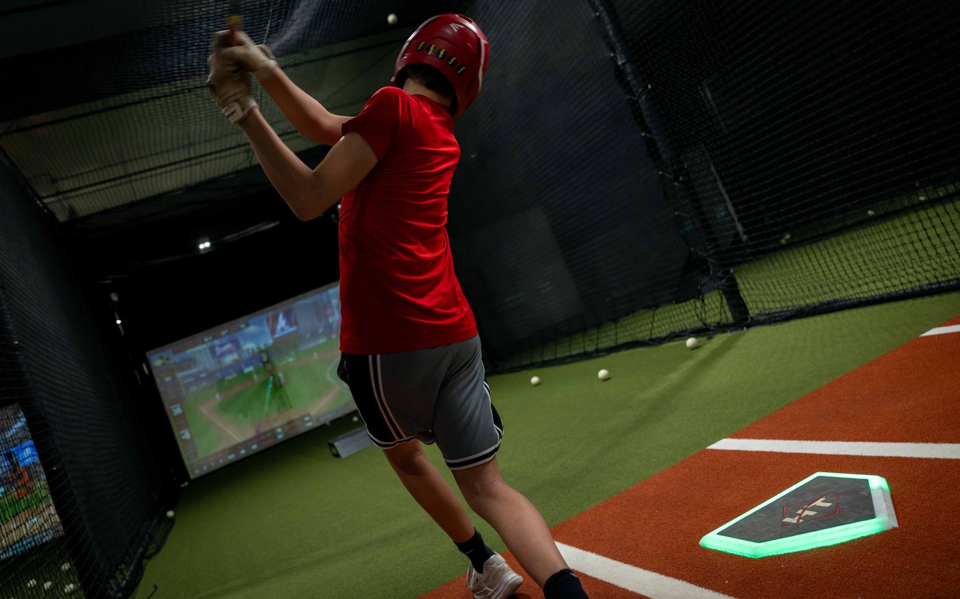 A player mid-swing in the batting cage under the lights