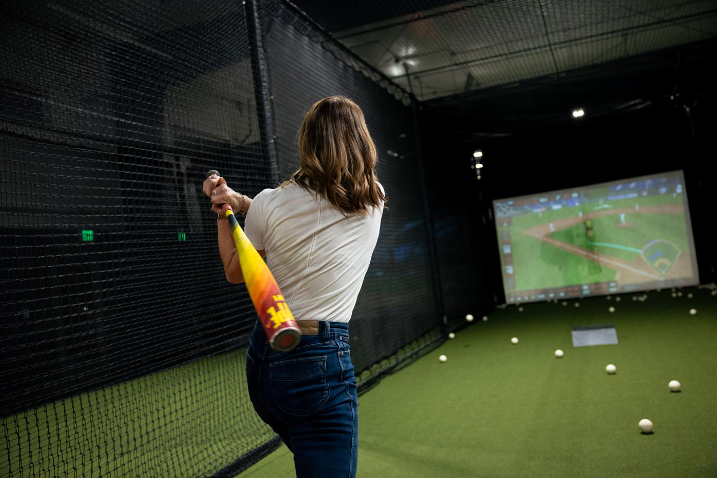 A guest lining up a swing toward the Hittrax simulator screen inside a Hitters batting cage